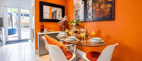 A dining area with a glass table, white chairs, and orange cushions.