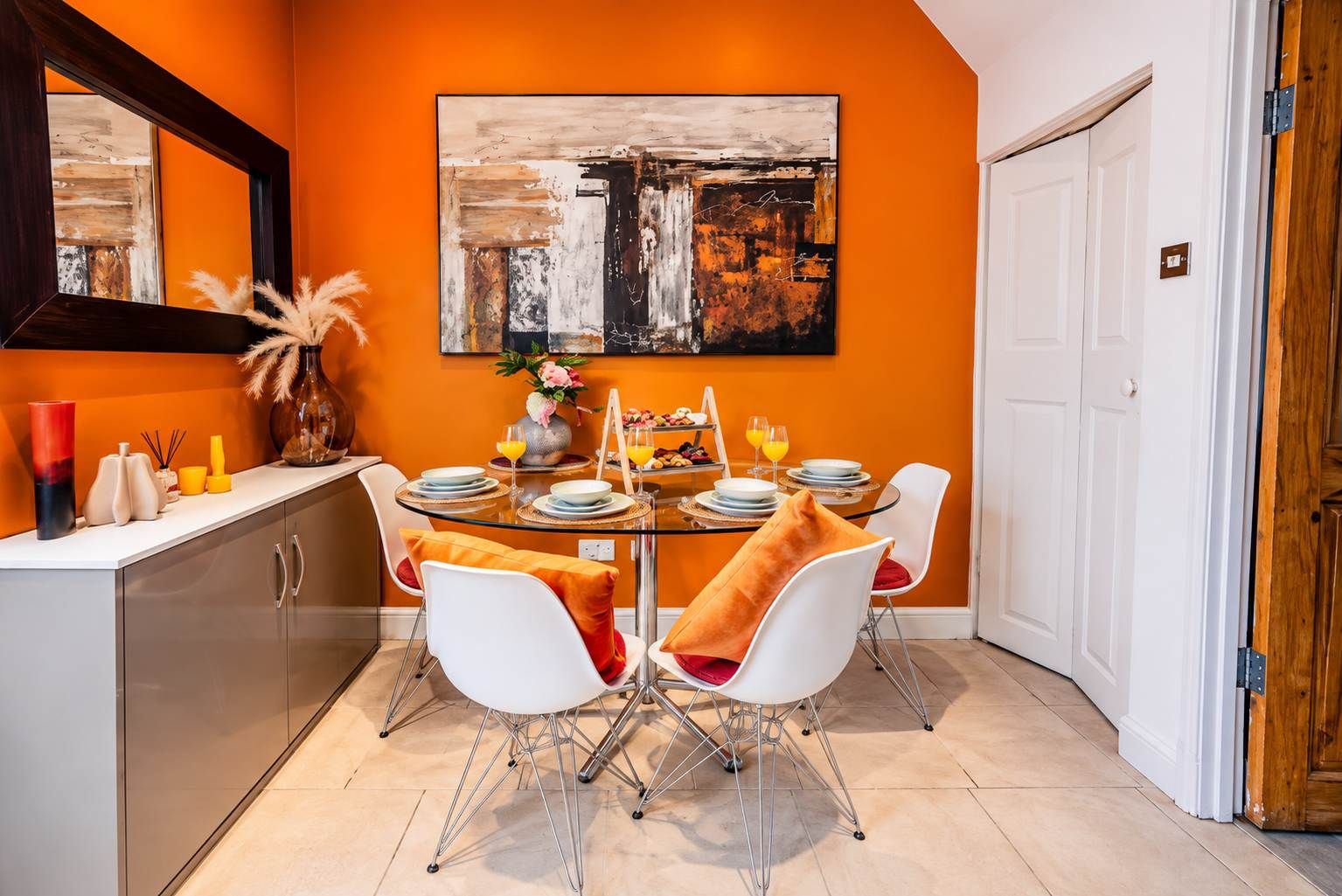 Un coin repas avec une table en verre, des chaises blanches et un grand tableau abstrait accroché au mur.