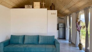 Ein Zimmer mit einem blaustumblauen Sofa, Holzboden und einer Küchenzeile, mit Blick durch große Fenster.