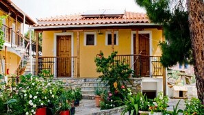 A yellow building with a tiled roof, a wooden door, and a small porch with potted plants. - viila kavourakia Studio - Garden View (4CRX+VJ Skiathos, Magnisias)