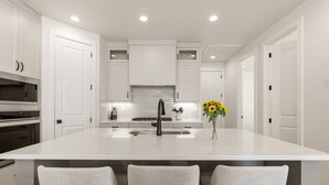 Una cocina moderna con armarios blancos, una isla central con pileta y tres sillas tipo barra.