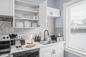 A kitchen with white cabinets, a tiled backsplash, a stainless steel sink, and a window with blinds.