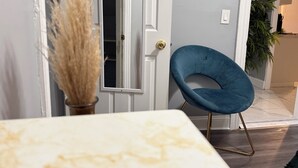 A room with a white door, a blue chair, a vase with dried plants, and a marble table.