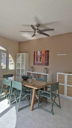 A dining area with a table, chairs, a ceiling fan, a cabinet, and a painting on the wall.