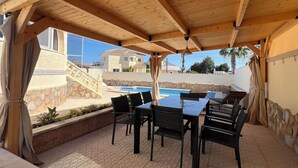 En uteplats med pool, en träpergola och murar av sten.