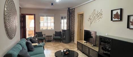 Un salón con sofá, sillas, una mesa de centro, televisor y decoración mural.