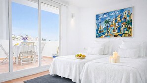 A hotel room with a balcony, a bed with white linens, a painting on the wall, and a bowl of fruit on the bed. - Lavender House - Hacienda 37 by Casasol (Nerja)