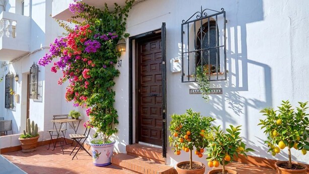 Un bâtiment blanc avec une porte en bois, des plantes en pot et une table à l’extérieur.