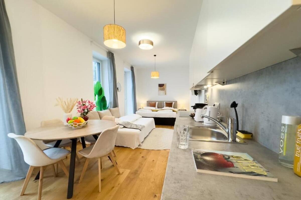 A modern kitchen with a dining area, a small living space, and a visible window.