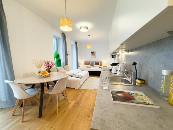 A modern kitchen with a dining area, a small living space, and a visible window. - Vienna Hills Living (Vienna)