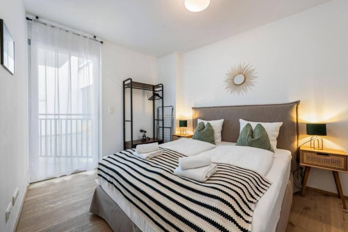 A neatly made bed with striped bedding, a bedside table with a lamp, and a wall-mounted mirror.
