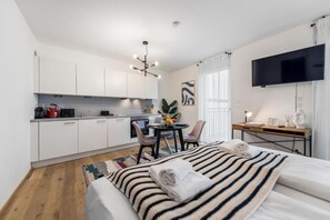 A modern hotel room with a bed, a desk, a TV, a kitchenette, and a dining area. - Vienna Hills Living (Vienna)