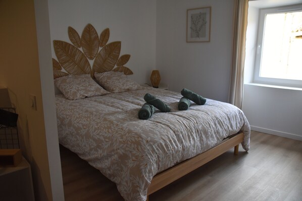 A bedroom with a bed, a headboard with leaf designs, a bedside table, and a window.