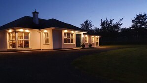 Une maison à deux étages, dotée d’un éclairage extérieur soigné, de grandes fenêtres et d’une cheminée.