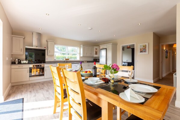 A modern kitchen with white cabinets, a dining table set for four, and a view of the garden through the window.
