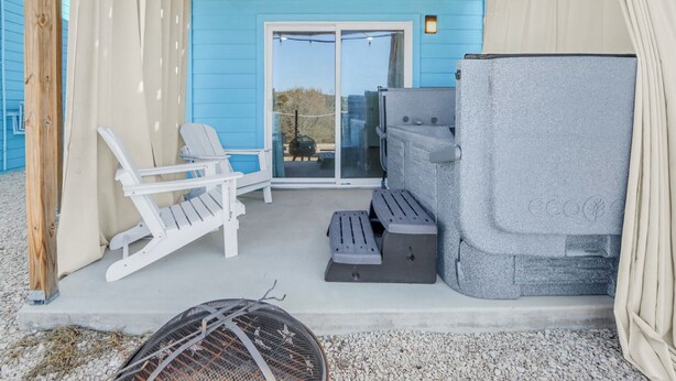 Un espace extérieur abrité, doté d’un mur bleu, de chaises blanches, d’un barbecue et d’un grand objet gris.