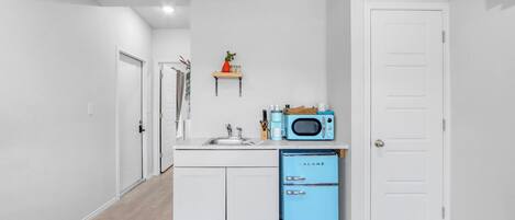 Une cuisine de taille réduite, avec des meubles blancs, un réfrigérateur bleu et un four à micro-ondes posé sur le plan de travail.