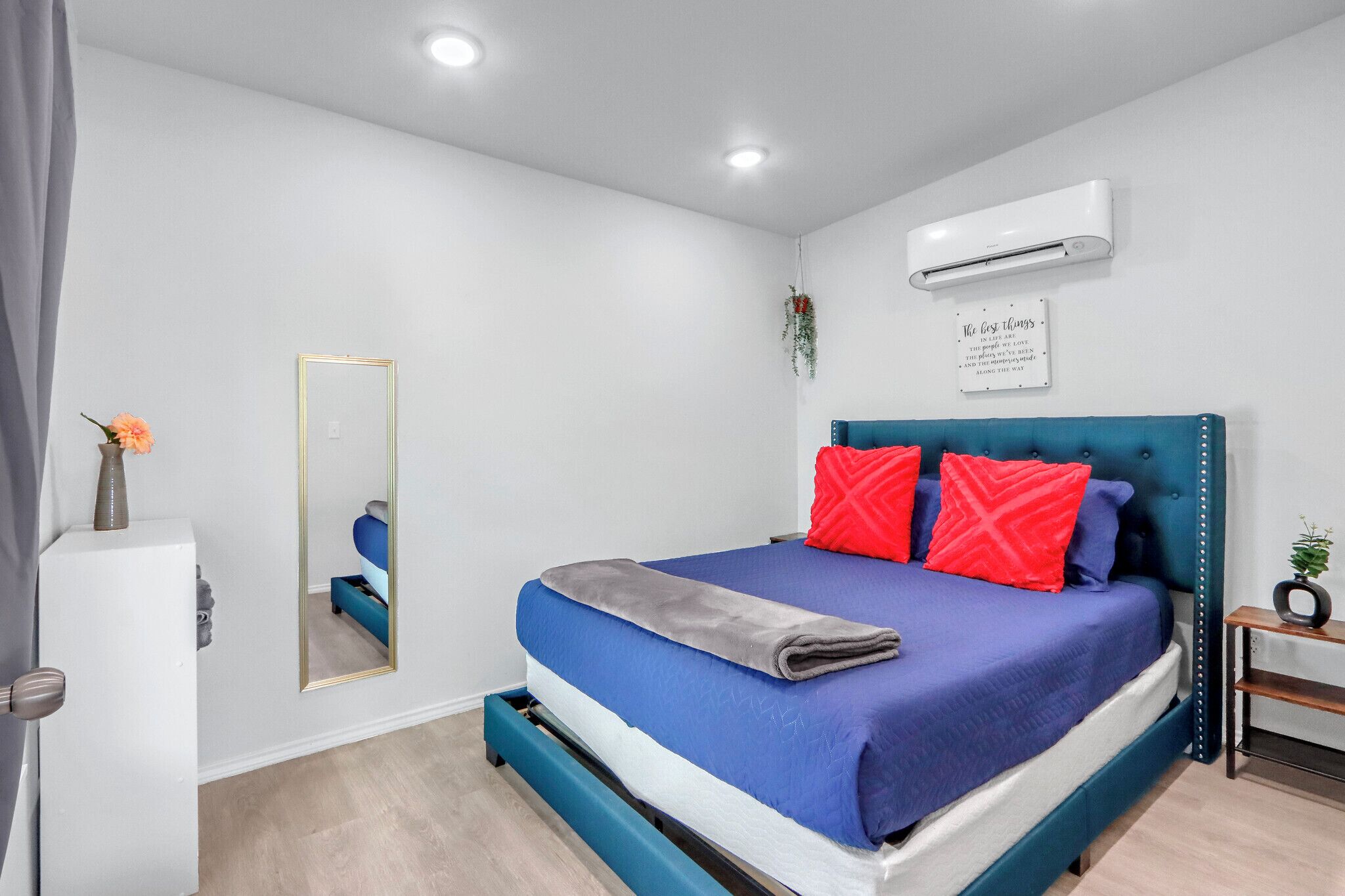 Une chambre à coucher moderne avec un lit, un miroir, un climatiseur et une petite plante posée sur une table de chevet.