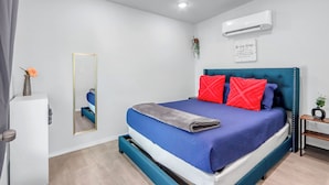 Une chambre à coucher moderne avec un lit, un miroir, un climatiseur et une petite plante posée sur une table de chevet.