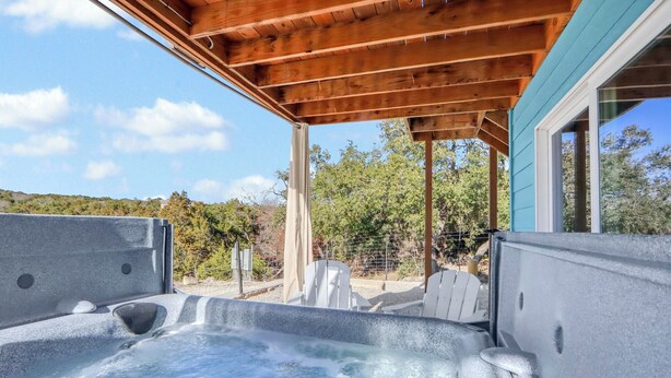 Een hottubgedeelte met een houten pergola erboven, omringd door een hek en bomen.