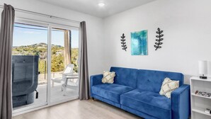 Een moderne woonkamer met een blauwe bank, een witte stoel en een glazen schuifpui naar een terras.