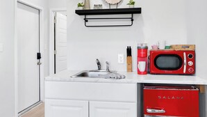 Una cocina con encimera blanca, microondas rojo, un fregadero y un estante negro sobre la encimera.