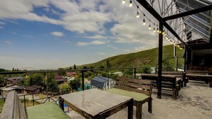 An outdoor seating area with tables and benches, a view of a hilly landscape, and a building with a sloped roof. - Olive Ala-Archa Hotel & SPA (Kashka-Suu)