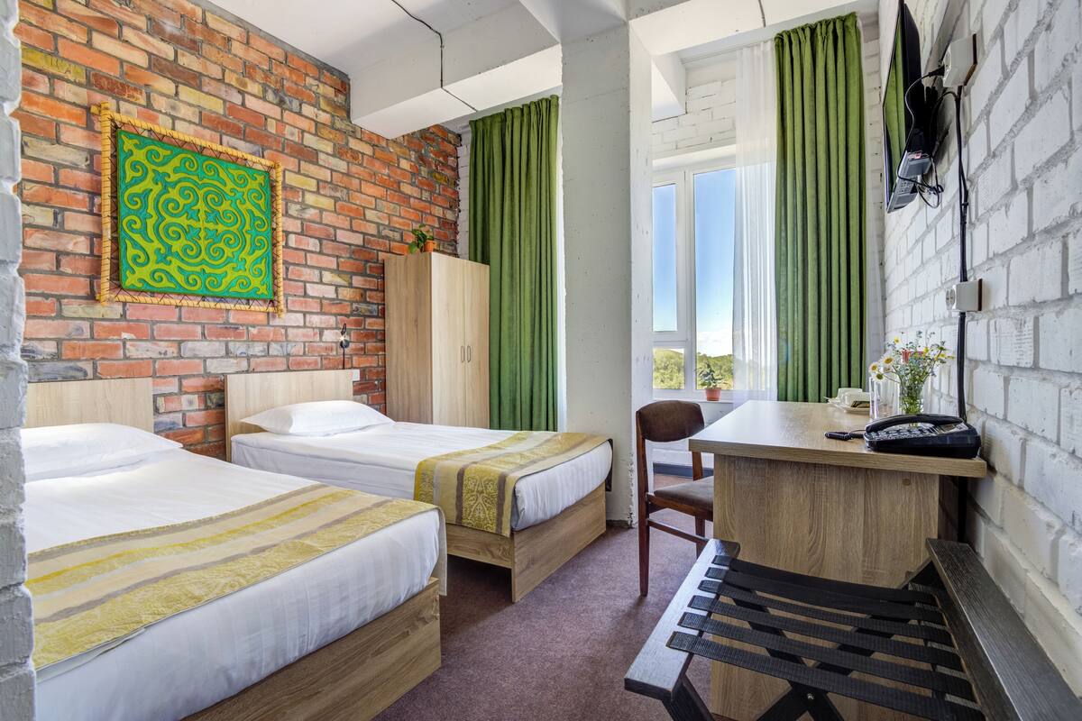 A hotel room with two beds, a desk, a chair, and a view of the outdoors.