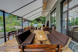 Een terras met houten banken en tafels, omgeven door stenen muren en grote ramen.