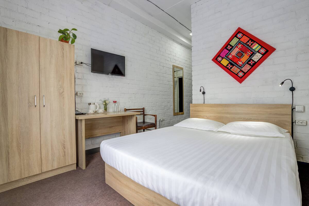 A bedroom with a bed, a desk, a chair, a wardrobe, a TV, and a wall-mounted quilt.