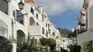 A narrow street with white buildings, a tiled pathway, and some greenery. - Verano Azul 96 Casa Monica by Casasol (Nerja)