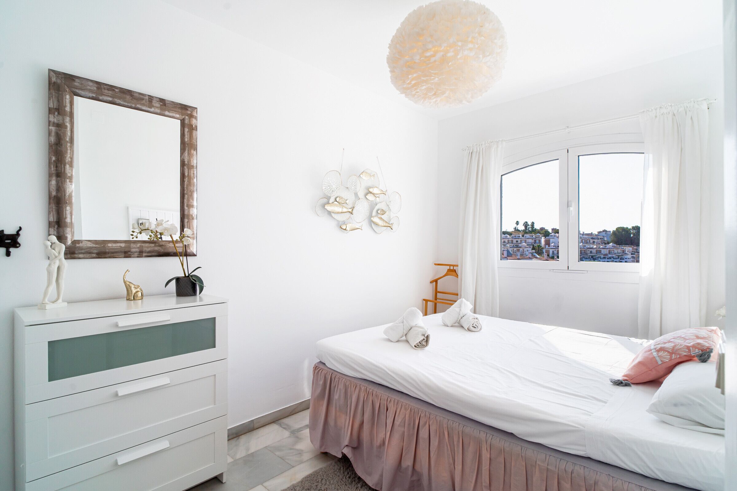 Een slaapkamer met een bed, een dressoir, een spiegel en een raam met uitzicht.