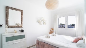 A bedroom with a bed, a dresser, a mirror, and a window with a view. - Verano Azul 96 Casa Monica by Casasol (Nerja)