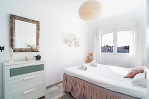 A bedroom with a bed, a dresser, a mirror, and a window with a view. - Verano Azul 96 Casa Monica by Casasol (Nerja)