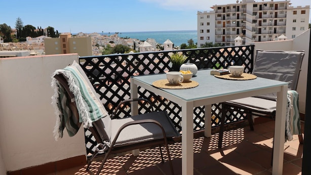 A balcony with a table, chairs, and a view of the sea and buildings. - Verano Azul 96 Casa Monica by Casasol (Nerja)