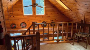 A wooden cabin with a sloped ceiling, a ceiling fan, a window, and a small balcony with a railing. - Hoel Pond Hideaway@Saranac Inn (Saranac Lake)