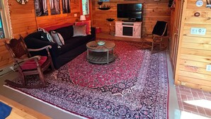 A wooden cabin interior with a living room featuring a sofa, chairs, a TV, and a fireplace. - Hoel Pond Hideaway@Saranac Inn (Saranac Lake)