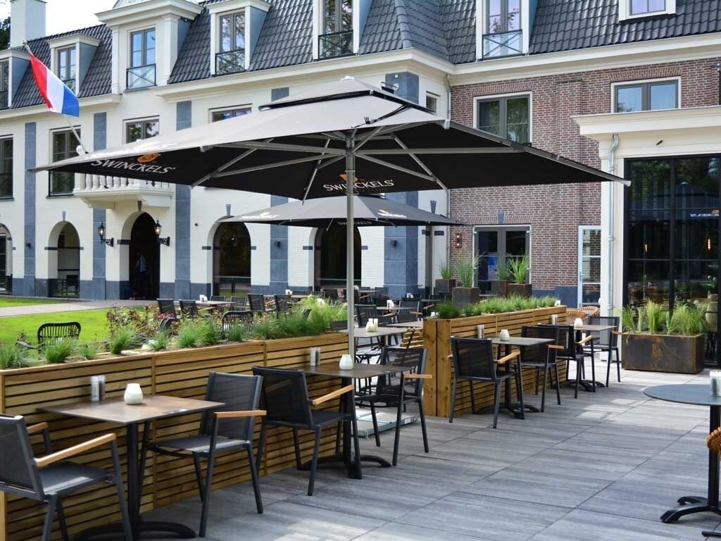 Un espace extérieur aménagé avec des tables et des chaises, un grand parasol, et un bâtiment en arrière-plan.