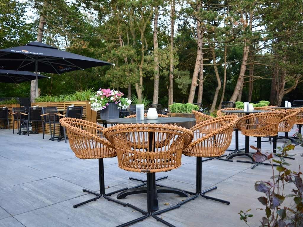 Espace extérieur aménagé avec des chaises et une table en osier, entouré d’arbres.