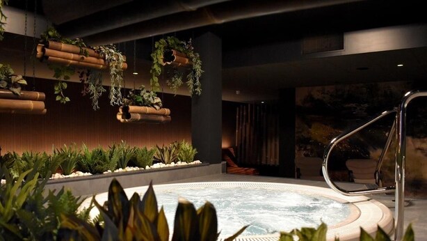 Un bain à remous entouré d’une végétation luxuriante, avec une personne se relaxant à l’arrière-plan.