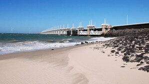 Une plage bordée d’une côte rocheuse, une longue jetée qui s’avance dans l’eau et, au loin, des éoliennes.