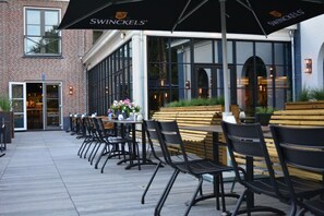 An outdoor seating area with tables and chairs, a brick building, and a glass door entrance. - Always a Great Idea To Unwind! Free Breakfast and Parking, Near Nature and Dunes (Burgh-Haamstede)