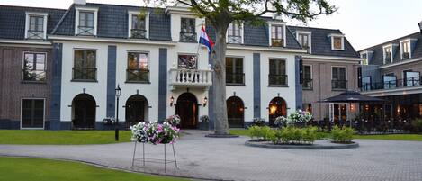A large, historic building with a central entrance, multiple windows, and a flag.