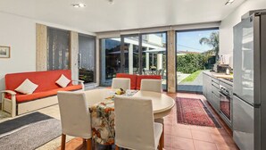 Ein moderner Wohnraum mit Sofa, Esstisch, Stühlen, Küchenzeile und großen Schiebeglasüren zum Außenbereich.