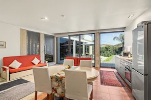 Um espaço de estar moderno com sofá, mesa de jantar, cadeiras, cozinha e grandes portas de vidro deslizantes que dão para um pátio externo.
