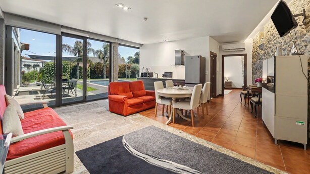 Ein geräumiger Wohnbereich mit einer Couch, einem Esstisch und Stühlen, eine Küche mit modernen Geräten und große Schiebeglastüren, die auf eine Terrasse führen.
