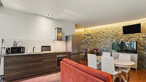 Eine moderne Küche mit Steinwand, einem Flachbildfernseher und einem Essbereich mit weißen Stühlen.