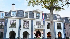 Un edificio grande de dos pisos con fachada simétrica, múltiples ventanas y una entrada central con balcón.