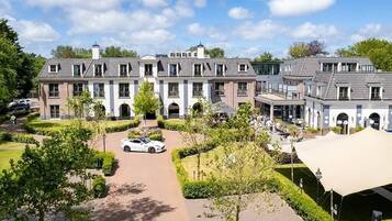 Een groot, meerijlaarig gebouw met een symmetrische gevel, een centrale oprit en een verzorgde tuin.