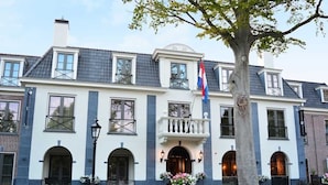 Un grand bâtiment à deux étages, doté d’une façade symétrique, de nombreuses fenêtres et d’une entrée centrale surmontée d’un balcon.